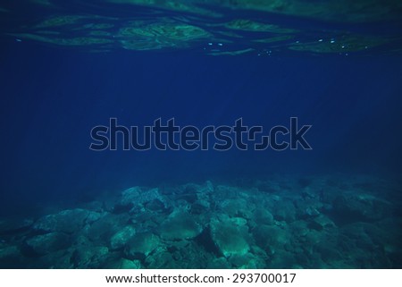 Underwater image showing reflections on the surface of the water, rocky bottom of the ocean and sun streaking through water.