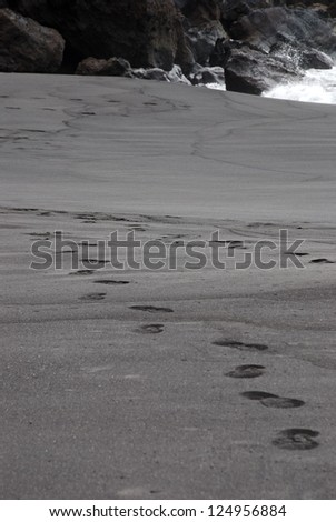footprint tracks in black sand as a black beach at the ocean