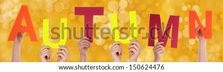 Many Hands Holding the Word Autumn with a Yellow Background