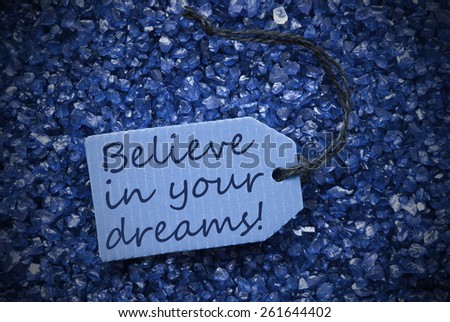 One Blue Label Or Tag With Black Ribbon On Blue And Purple Small Stones As Background With English Life Quote Believe In Your Dreams With Frame