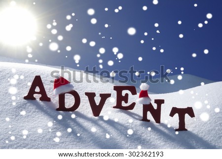 Red Wooden Letters With Santa Hat Building German Word Advent Means Christmas Time Or Season. Snow And Snowy Scenery With Snowflakes.Wooden Background. Sunny Christmas Atmosphere Sun And Blue Sky