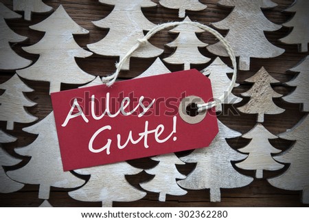 Red Christmas Label With Ribbon On Wooden Christmas Trees Background. Vintage Or Rustic Style. Label With German Text Alles Gute Means Best Wishes For Christmas Or Season Greetings.Close Up Or Macro