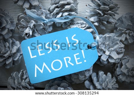 One Light Blue Label On Fir Cones And White Wooden Background. English Life Quote Less Is More Vintage Or Retro Style Used As Winter Or Christmas Background With Frame