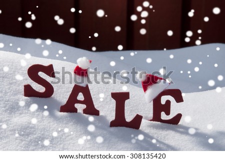 Red Wooden Letters With Santa Hat Building Word Sale In Christmas Time Or Season Snow And Snowy Scenery With Snowflakes In Front Of Red Wooden Background. Christmas Atmosphere