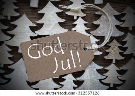 Brown Christmas Label With Ribbon On Wooden Christmas Trees Background. Vintage Style. Label With Swedish Text God Jul Means Merry Christmas For Christmas Or Season Greetings.Close Up Or Macro