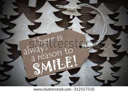 Brown Christmas Label With Ribbon On Wooden Christmas Trees Background. Vintage Style. Label With English Quote There Is Always A Reason To Smile For Christmas Or Season Greetings.Close Up Or Macro