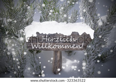 Wooden Christmas Sign With Snow And Fir Tree Branch In The Snowy Forest. German Text Herzlich Willkommen Means Welcome For Seasons Greetings Or Christmas Greetings. Christmas Atmosphere With Snowflake