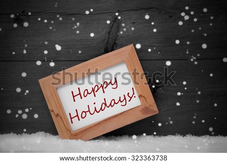 Gray Christmas Card With Brown Picture Frame On White Snow With Snowflakes. English Text Happy Holidays. Rustic Wooden, Retro Vintage Background. Black And White
