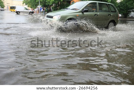 A car splashes through a large puddle on a wet road.