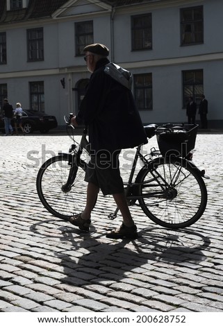 RIGA, LATVIA - AUGUST 9, 2010: Man walking his bicycle on an old cobblestone road in Old Town of Riga