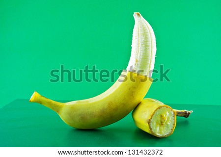 Banana half peeled lies against a green background