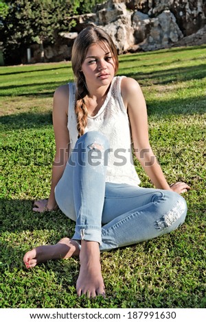 Barefoot girl in ripped jeans sitting on the grass in the park against the rocks