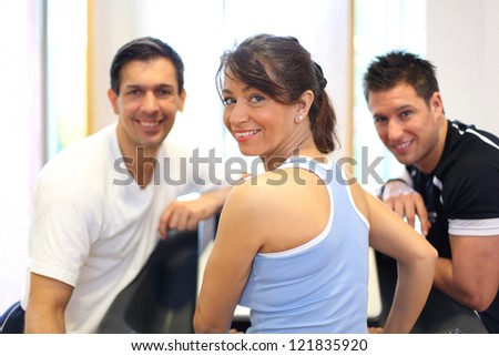 Group of two men and one woman on a treadmill in a gym smiling into the camera