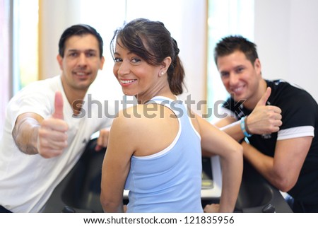 Group of two men and one woman on a treadmill in a gym giving thumbs up