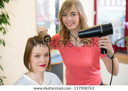 Hairdresser with a barrel brush and a blow-dryer styling a customers hair