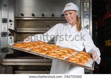 baker posing with baking tray full of pretzels in front of the oven