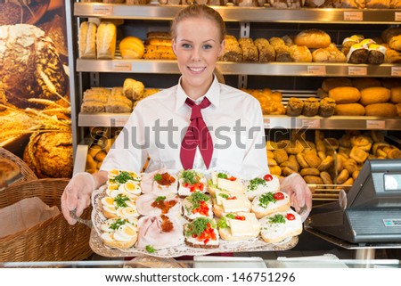 Shopkeeper in bakery or baker\'s shop presenting tablet with sandwiches, cold cut, cheese, cold meat and egg.