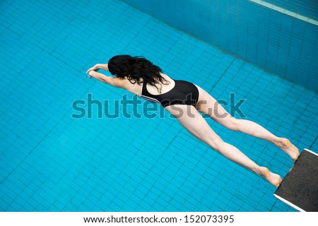 Woman jumping from a diving board at public swimming pool