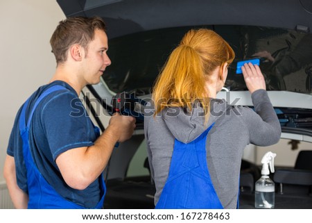 Worker in garage tinting a car window with tinted foil or film