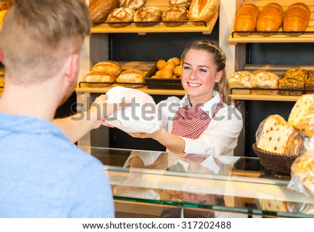 Shopkeeper or saleswoman in bakery hand bag of bread to customer