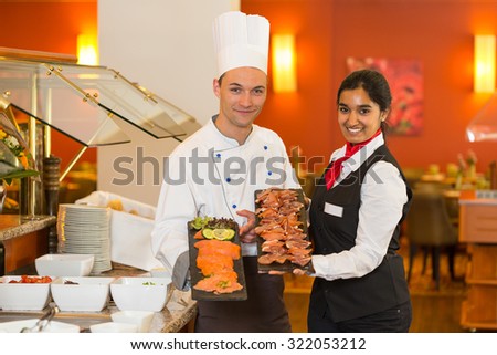 cook or chef and waitress posing with cold meat at buffet in restaurant
