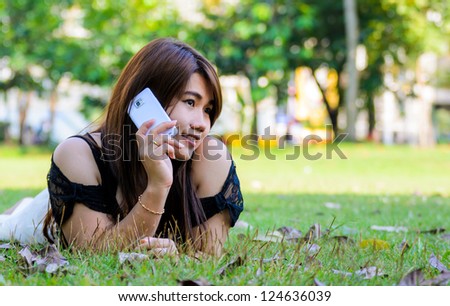 Beautiful young woman lies on green summer meadow among clover and talks by mobile phone.