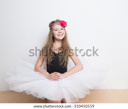 Adorable little girl with a long hair and a flower head band, wearing a white tutu skirt in a studio