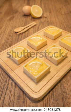 Fresh delicious lemon tart dessert presented nicely on wooden cutting board.