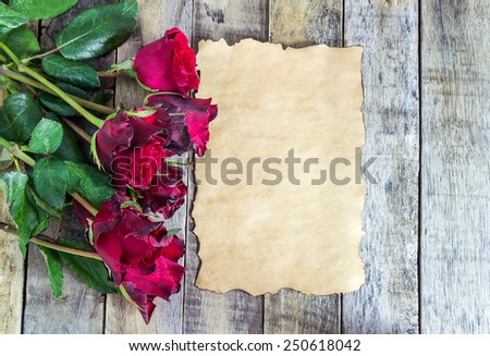 Fresh red rose and old paper on a wooden background. Holidays romantic background