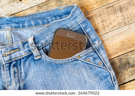 Smart phone in pocket blue jeans on wooden background
