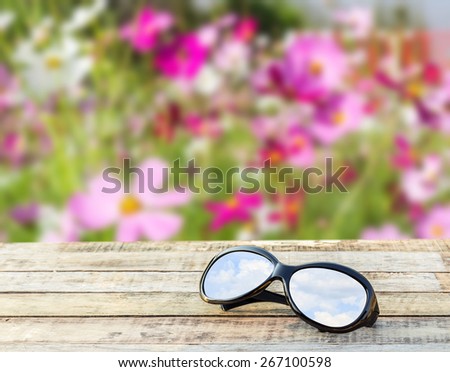 Clear sky in eyeglasses on the wooden table over blurred flower background