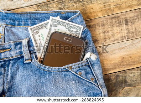 Dollar money and smart phone in pocket blue jeans on wooden background