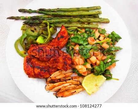 White dinner plate with grilled chicken,  asparagus, green peppers, spinach salad, jimaca potatoes and lime