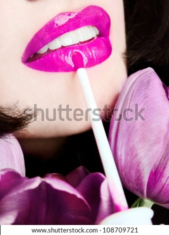Sexy pretty young woman applying pink lip gloss / lipstick on her lips / pink flowers / tulips