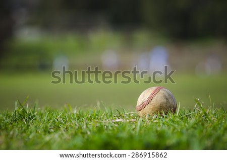 Used baseball laying on fresh green grass with baseball players in the background