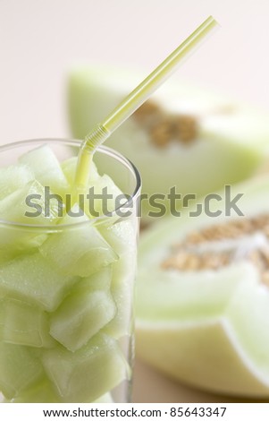 Green honeydew melon pieces in a glass with straw and blurred melon in background