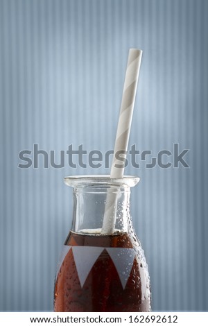 A single cola soda pop retro bottle and straw on blue background