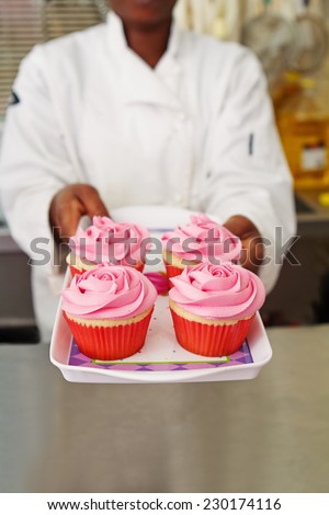 Pastry chef offering a tray of pink rose cupcakes