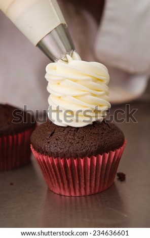 Whipped cream frosting being piped onto a chocolate cupcake