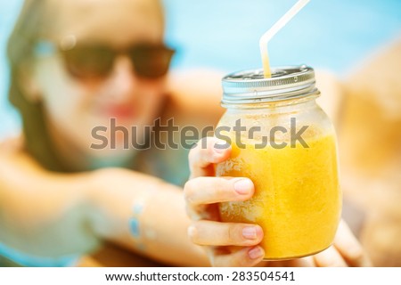 Fruit smoothie - healthy eating concept. Close up of  detox smoothie with mango. Woman hand with gold sticer tatto holding mango smoothies outside on the pool.