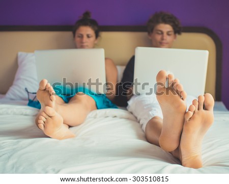 An attractive young couple work on their laptops in bed