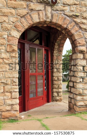 A bright red door and arched entry in an old sandstone building that was once a grocery store.
