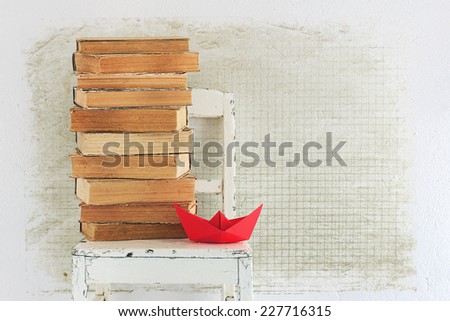 Background with old books, chair and red paper boat