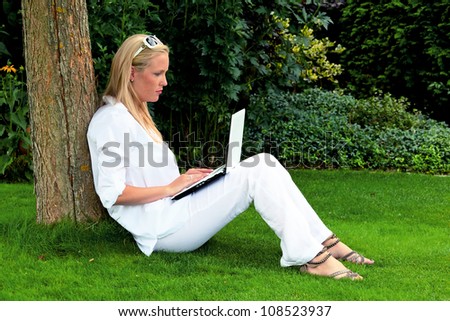 a young woman sitting with a laptop computer in the garden and surf the internet. wi-fi in the park