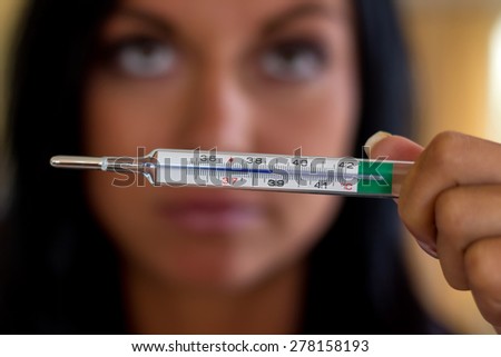 a woman holding a clinical thermometer. symbolic photo for sick and fever
