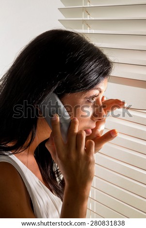 a young woman watching something through the blinds of her window