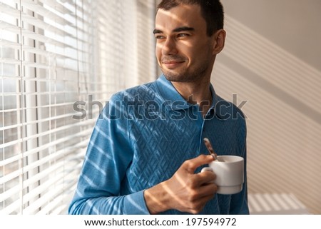 Young Man With Cap of Coffee (smiling young man with cup of coffee looking out the window)