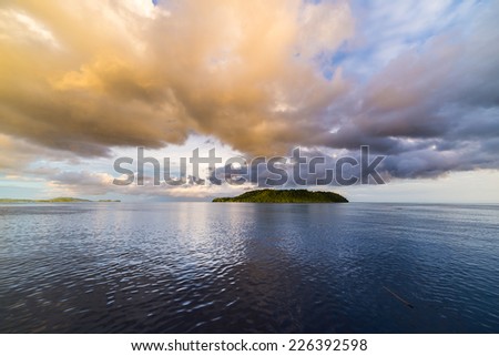 Deep blue sea and dramatic sky with colorful clouds at dusk in the remote Togean Islands, Central Sulawesi, Indonesia. Wide angle view from offshore.