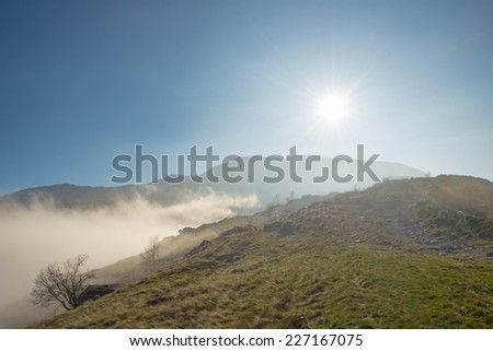 Clouds and fog gathering on the mountain ridge in a sunny afternoon. Wide angle shot in backlight in the italian western Alps.