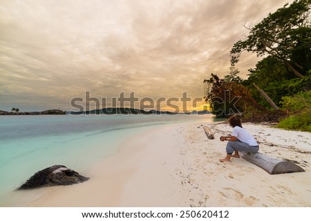 Tourist watching a relaxing sunset sitting on the beach in the remote Togean Islands, Central Sulawesi, Indonesia, upgrowing travel destination in recent years. Wide angle view.